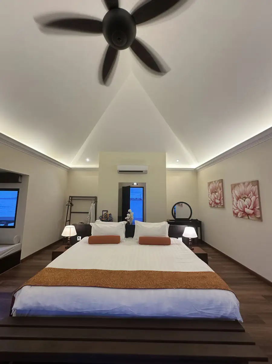 A plush bed inside a bright bedroom at Sea Star Resort near the Tun Sakaran Marine Park facing a window with partial sea views, a wooden daybed, warm wooden plank floors, and air conditioning.