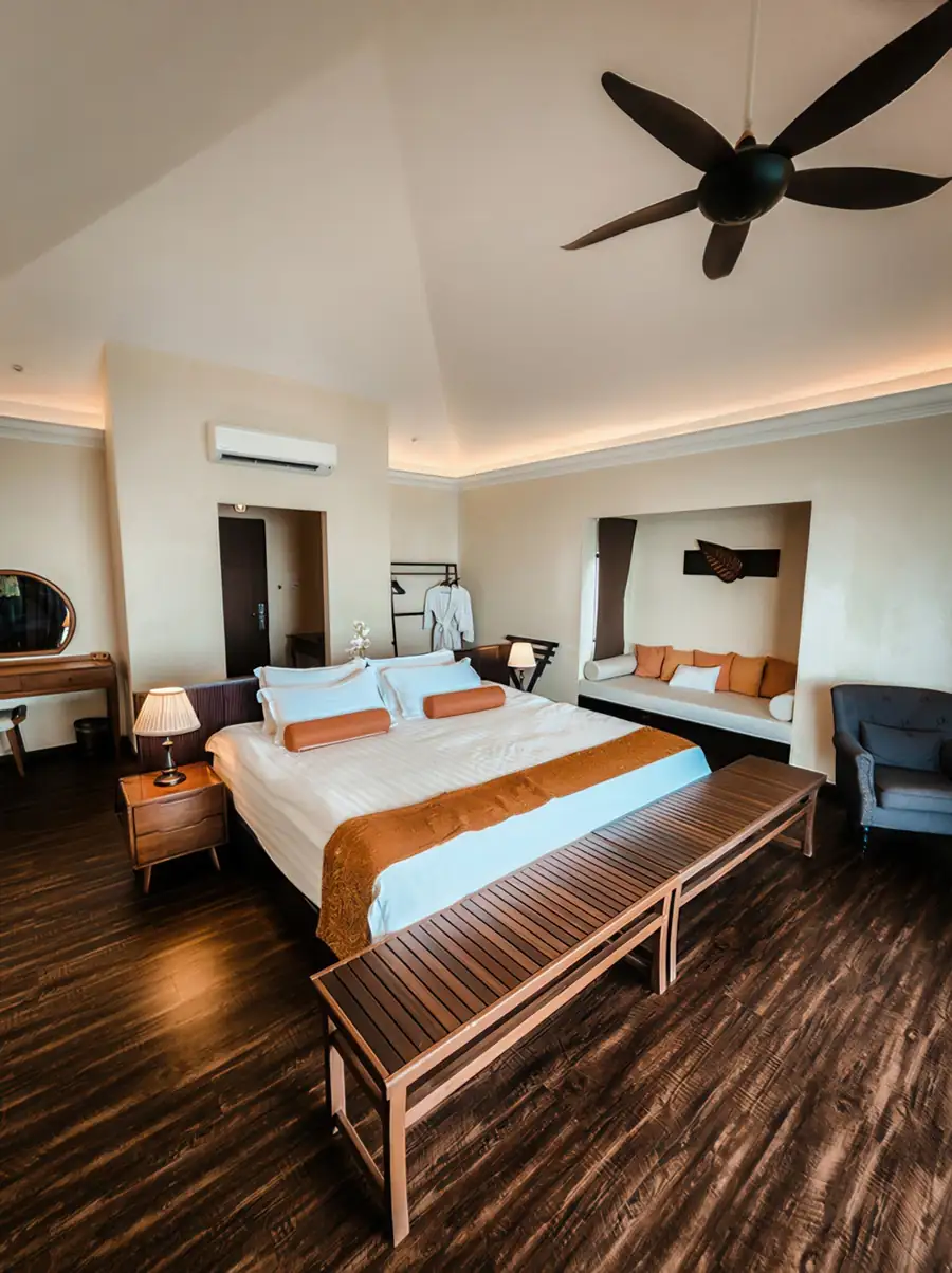 A spacious bedroom at Sea Star Resort near the Tun Sakaran Marine Park showcasing a large bed, a daybed alcove, vanity desk, dark polished timber flooring, and air conditioning.